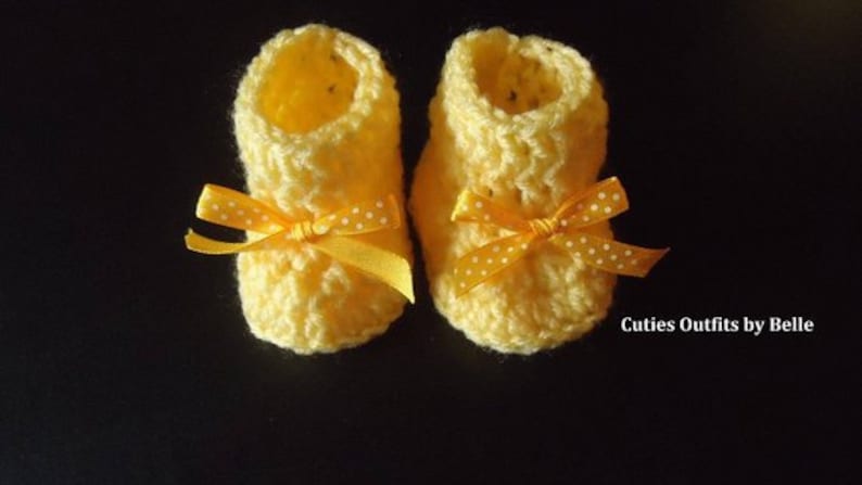 May include: A pair of yellow crocheted baby booties with yellow and white polka dot bows.