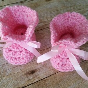 May include: A pair of pink crocheted baby booties with white satin ribbon bows.