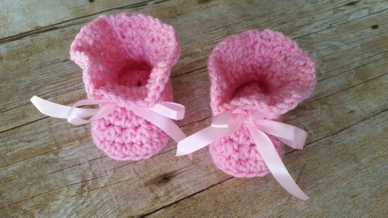 May include: A pair of pink crocheted baby booties with white satin ribbon bows.