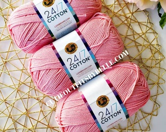 May include: Three pink balls of Lion Brand 24/7 Cotton yarn. The yarn is a light pink color and is perfect for knitting or crocheting.