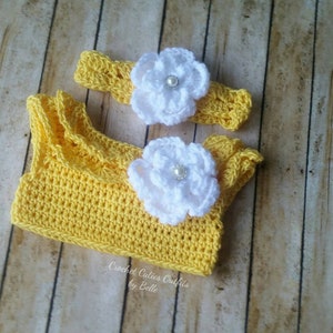 Peut inclure: Ensemble de crochet jaune pour b&eacute;b&eacute;, comprenant un haut et un bandeau. Le haut est orn&eacute; de volants, et les deux pi&egrave;ces sont d&eacute;cor&eacute;es de fleurs blanches avec des perles en leur centre. Le texte "Crochet Cuties Outfits by Belle" est visible.