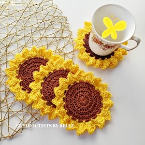 Pu&ograve; includere: Quattro sottobicchieri all'uncinetto a forma di girasole, di colore giallo e marrone. I sottobicchieri sono impilati uno sopra l'altro. I sottobicchieri sono su una superficie di metallo dorato.