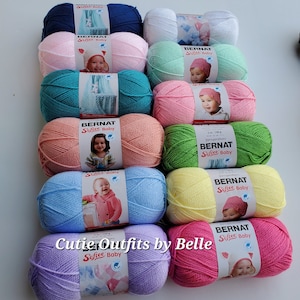 May include: A collection of ten skeins of Bernat Softee Baby yarn in various pastel colors, including lavender, pink, yellow, light blue, and green. Each skein has a label with the Bernat Softee Baby logo and a picture of a baby wearing a crocheted hat.