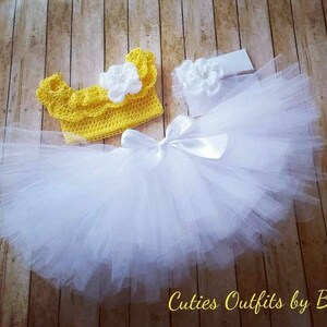 Peut inclure: Un ensemble pour b&eacute;b&eacute; ou enfant compos&eacute; d'un haut en crochet jaune avec une fleur blanche, d'une jupe en tulle blanche avec un n&oelig;ud en satin et d'un bandeau blanc assorti avec une fleur.