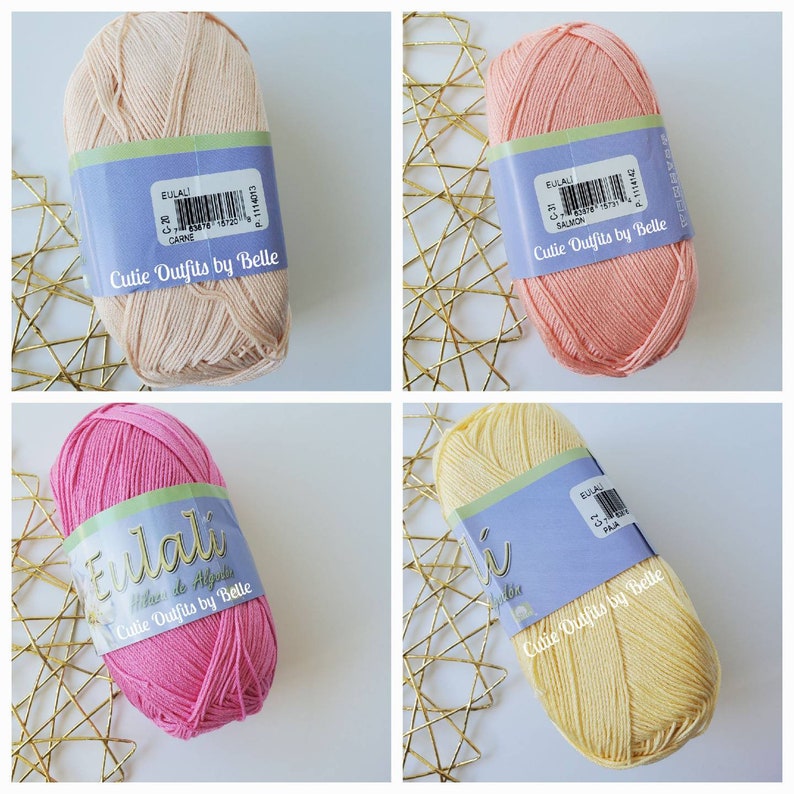 May include: Four skeins of yarn in various colors: light peach, salmon, hot pink, and pale yellow. Each skein has a label that reads "Eulali" and "Cutie Outfits by Belle". The yarn is displayed on a gold geometric patterned surface.