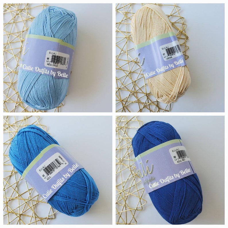 May include: Four skeins of yarn in various colors: light blue, cream, medium blue, and dark blue. Each skein has a label that reads "EULALI" and "Cutie Outfits by Belle". The yarn is arranged on a gold-colored, geometric patterned surface.