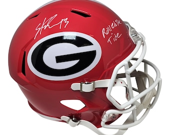 May include: A red football helmet with a white facemask. The helmet features a large black and white "G" logo and handwritten signatures. The text "Roll Tide" is also visible on the helmet.