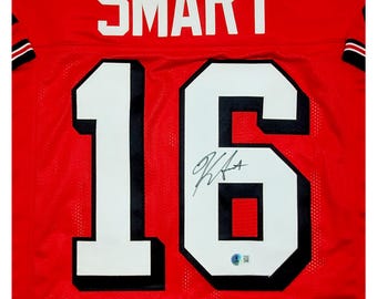 May include: Red football jersey with the name "SMART" and the number "16" on the back. The jersey is signed in black ink.