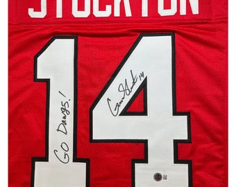 May include: Red hockey jersey with the name "STOCKTON" and the number "14" on the back. The jersey is signed by the player with the text "Go Dawgs!" and "G. Stockton 14" in white.