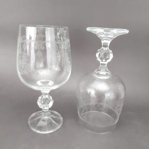 May include: Two clear, stemmed wine glasses. One glass is upright, the other is upside down. The upright glass has etched floral designs on the bowl. Both glasses have a faceted ball on the stem and a round base.