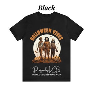 May include: Black t-shirt with a graphic of three people in front of a full moon with the text "Halloween Vibes" above them and "Designs by LCG" and "www.designsbylcg.com" below them.