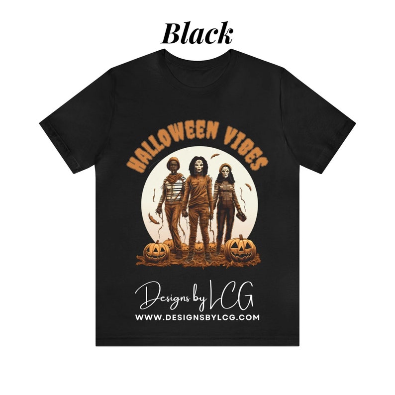 May include: Black t-shirt with a graphic of three people in front of a full moon with the text "Halloween Vibes" above them and "Designs by LCG" and "www.designsbylcg.com" below them.