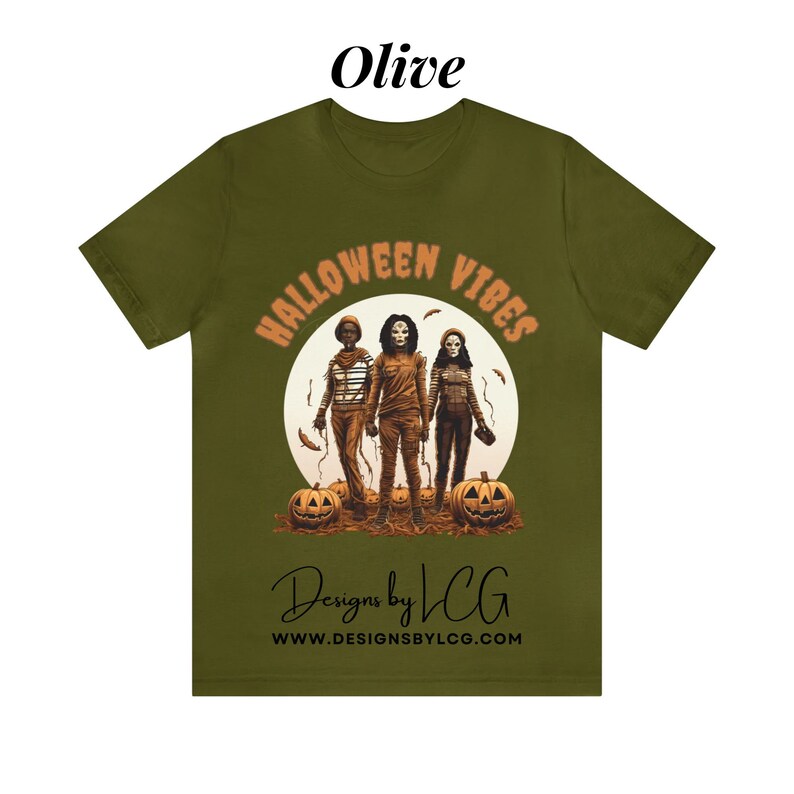 May include: Olive green t-shirt with a graphic of three figures in front of a full moon with the text "Halloween Vibes" in orange and black. The text "Designs by LCG" and "www.designsbylcg.com" are printed below the graphic.
