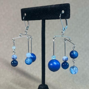 May include: A pair of silver mobile earrings with blue and white agate beads. The earrings are suspended from silver hooks.