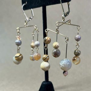May include: A pair of gold tone earrings with a mobile design featuring multiple round agate beads in shades of brown, beige, and gray.