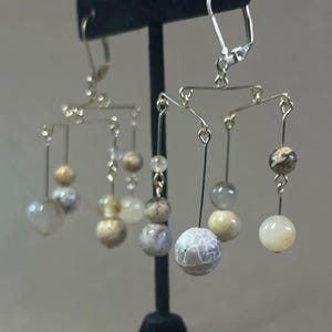 May include: A pair of silver earrings with a mobile design featuring multiple white and brown agate beads.