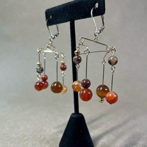 Könnte beinhalten: Ein Paar Hängeohrringe mit einem Mobile-Design. Die Ohrringe sind aus Golddraht gefertigt und haben Karneol-, Jaspis- und Achatperlen in Rot-, Orange- und Brauntönen.