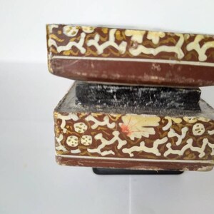May include: Two stacked wooden boxes with intricate gold and white floral designs. The boxes are brown and have a worn, antique look.