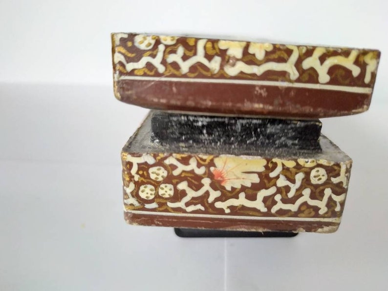 May include: Two stacked wooden boxes with intricate gold and white floral designs. The boxes are brown and have a worn, antique look.