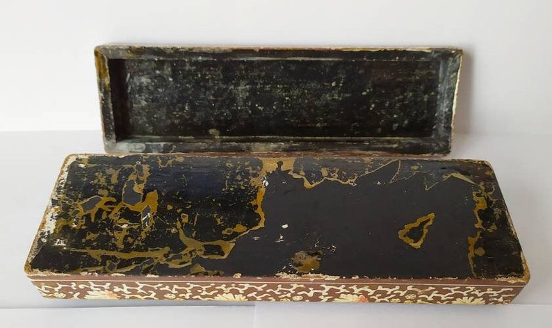 May include: An antique wooden box with a black interior and gold accents. The box is decorated with a floral pattern and has a hinged lid.