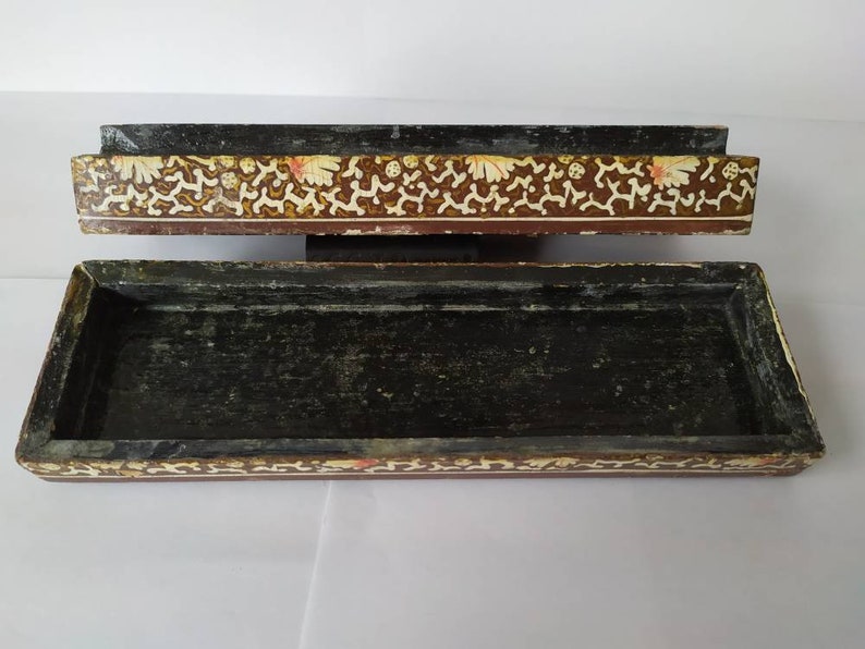 May include: A rectangular wooden box with a black interior and a decorative floral pattern on the top and bottom edges. The pattern is in shades of brown, gold, and white.