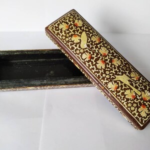 May include: A rectangular wooden box with a brown base and a lid decorated with intricate floral patterns in white and orange. The box is open, revealing a black interior.
