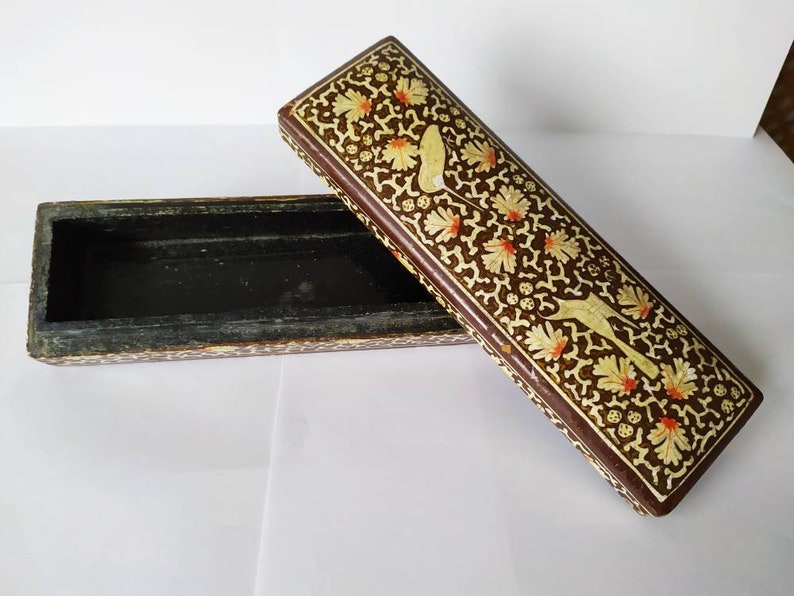 May include: A rectangular wooden box with a brown base and a lid decorated with intricate floral patterns in white and orange. The box is open, revealing a black interior.