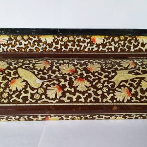 May include: A brown wooden box with a decorative floral design in gold and red. The box has a hinged lid and is decorated with intricate patterns.