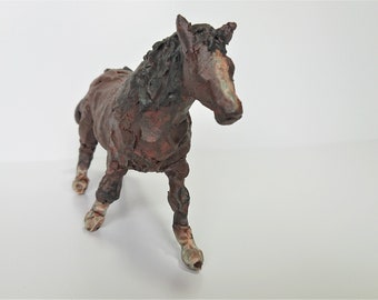 May include: A brown and black horse figurine with a textured surface. The sculpture has a detailed mane and tail, and is posed in a walking stance. The horse's hooves are a lighter color.