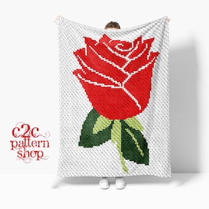 May include: A white crochet blanket with a red rose design. The blanket is held up by a person, and the text "C2C pattern shop" is visible in the lower left corner.