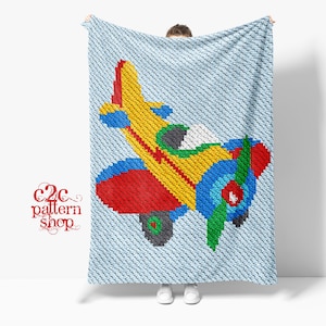 Könnte beinhalten: Eine Häkeldecke mit einem bunten Flugzeugmuster. Das Flugzeug ist gelb, rot, blau und grün. Die Decke ist hellblau.