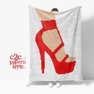 May include: A crochet pattern for a red high-heeled shoe. The pattern is displayed on a white blanket held by a person.