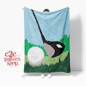 May include: A crocheted blanket with a golf-themed design. The blanket depicts a golf ball, club, and grass against a blue sky. The blanket is held up by a person. The blanket is blue, green, and white.