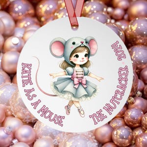 May include: A white round ornament with a pink and blue illustration of a girl dressed as a mouse from the Nutcracker. The text "Katie as a Mouse The Nutcracker 2021" is written around the illustration.