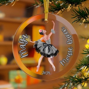 May include: A clear glass Christmas ornament with a ballerina in a gray and black tutu. The ornament has the text "Maya Mouse Queen 2024" on it.