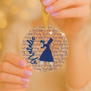 May include: A round, clear acrylic ornament featuring a repeating dark blue text pattern that reads Party Girl 2026. The center displays a graphic of a figure in a dark blue dress with a blue hair bow, and the name Natalie in blue script.