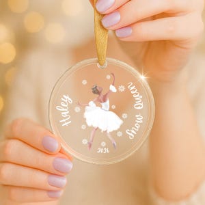 May include: Clear, round ornament with a gold ribbon. The ornament features a ballerina illustration with the text "Haley Snow Queen 2026". Snowflakes are scattered around the ballerina.