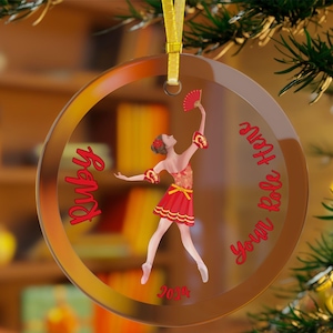 May include: A round glass ornament with a red and gold ballerina holding a fan. The ornament has the text "Ruby" and "You Rock,  Hope" on it. The year 2024 is also printed on the ornament.