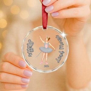 May include: A clear circular acrylic ornament hanging from a red ribbon. The center features an illustration of a child in a grey tutu and mouse ears. The text reads Stella, Lead mouse, and 2026 in black script and block lettering.