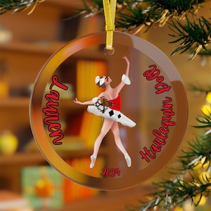 May include: A round glass ornament with a ballerina in a red and white costume. The ornament has the text "Lauren" and "Harlequin Doll 2024" on it.