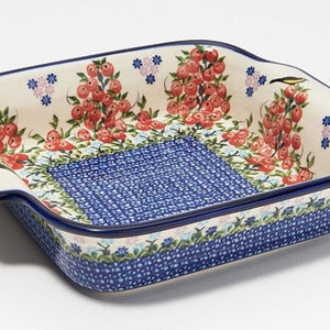 Puede incluir: Un plato para hornear cuadrado de cerámica con un patrón floral azul y blanco y bayas rojas. El plato tiene dos asas a los lados.