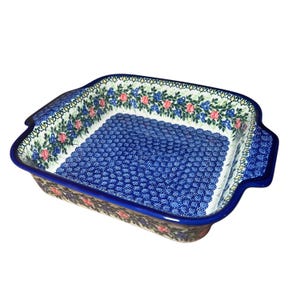 May include: A blue and white ceramic baking dish with a floral design. The dish has a square shape with rounded corners and two handles on the sides.