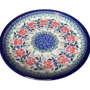 May include: A blue and white ceramic plate with a floral design. The plate has a blue border with a white Greek key pattern. The center of the plate features a blue and white floral design with pink flowers.