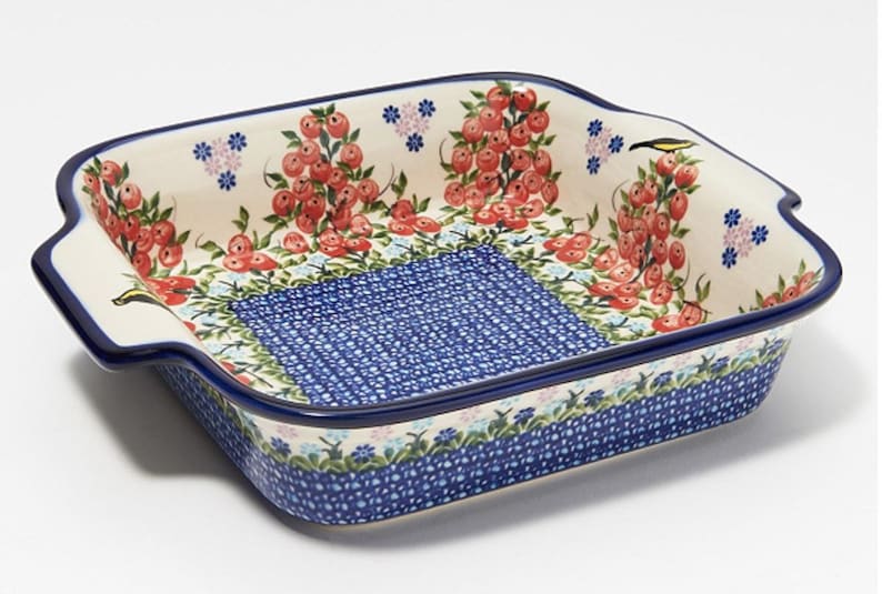 May include: A square ceramic baking dish with a blue and white floral pattern and red berries. The dish has two handles on the sides.