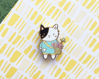 May include: A black and white cat wearing a light blue shirt and carrying a basket of flowers. The cat is a cartoon-style enamel pin.