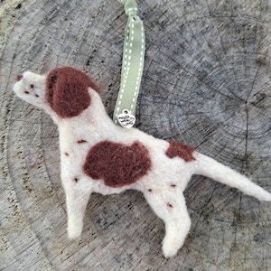 May include: A felt dog ornament in white and brown, with brown patches and head. It hangs from a green ribbon with white spots and a heart charm that says "made with love". A charming, handcrafted decoration.