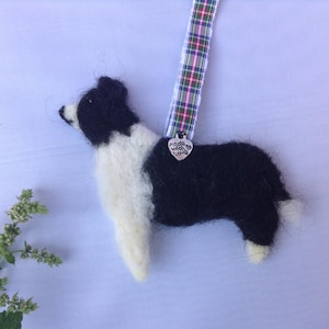 May include: A black and white felt border collie ornament with a silver charm that says "Made with love". The ornament is hanging from a red, green and white tartan ribbon.