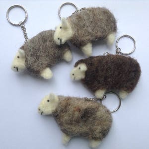 May include: Four felted sheep keyrings in various shades of brown and grey. Each sheep has a white face and legs, with a silver-coloured metal keyring attached. The sheep are handmade and fluffy.