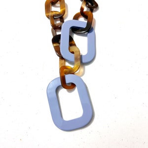 May include: A long necklace made of large, chunky links. The links are a mix of brown and light blue colors. The links are in the shape of squares and rectangles.