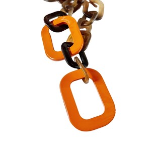 May include: A close-up of a chain made of orange, brown, and black plastic links. The links are in the shape of squares and rectangles. The chain is hanging from the top of the image.